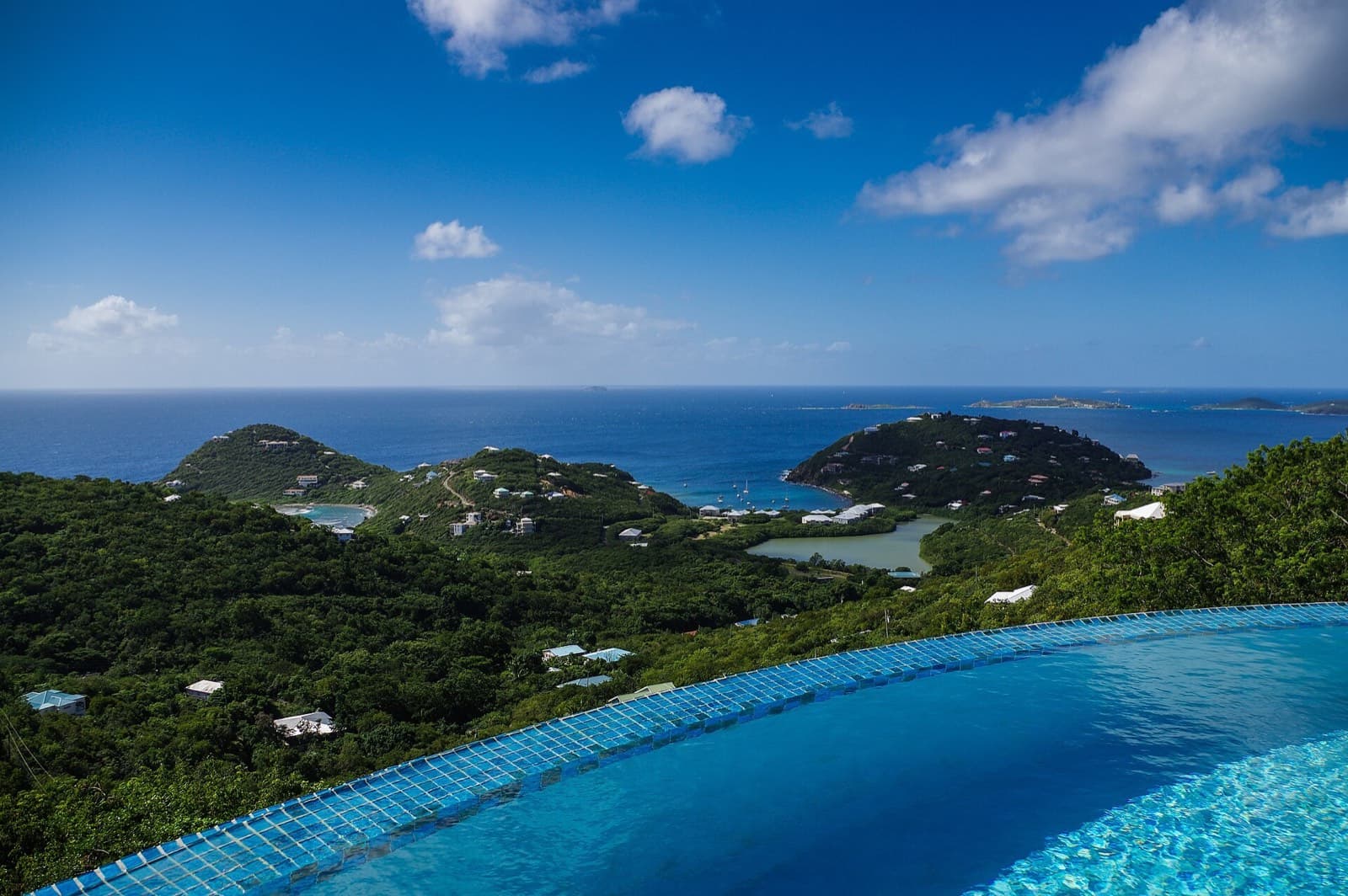 Imagen ilustrativa: alberca infinita redonda con vista a una bahía tropical, colinas verdes e islas