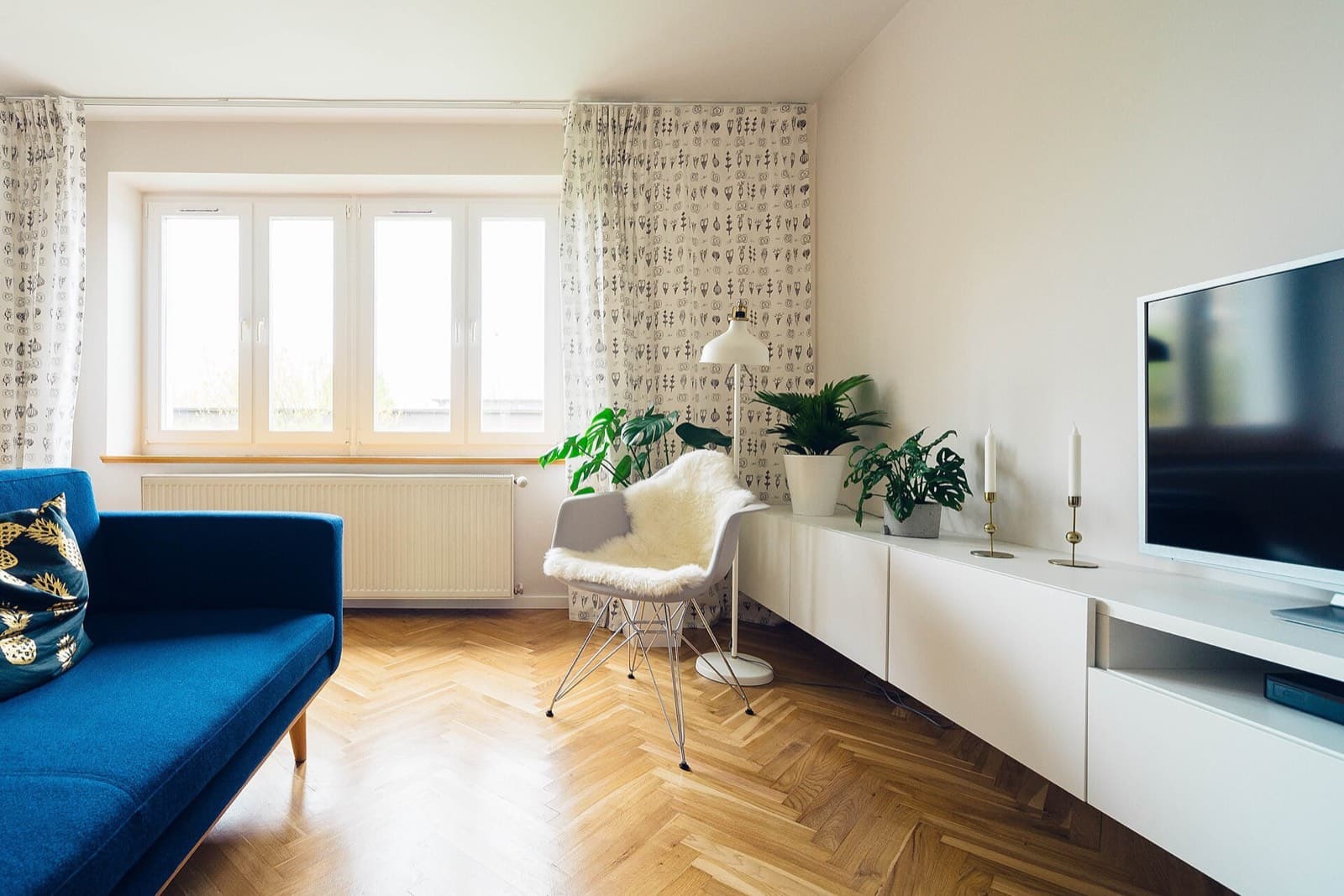 Imagen ilustrativa: sala luminosa con sofá azul, piso de madera en espiga, plantas y mueble blanco