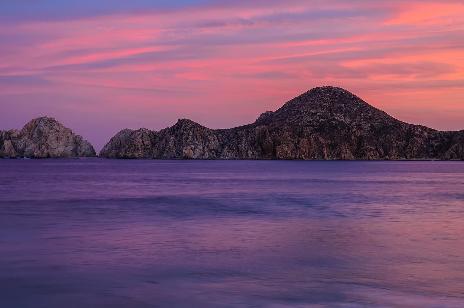 Atardecer rosa y violeta sobre el mar con los cerros rocosos de Cabo San Lucas al fondo