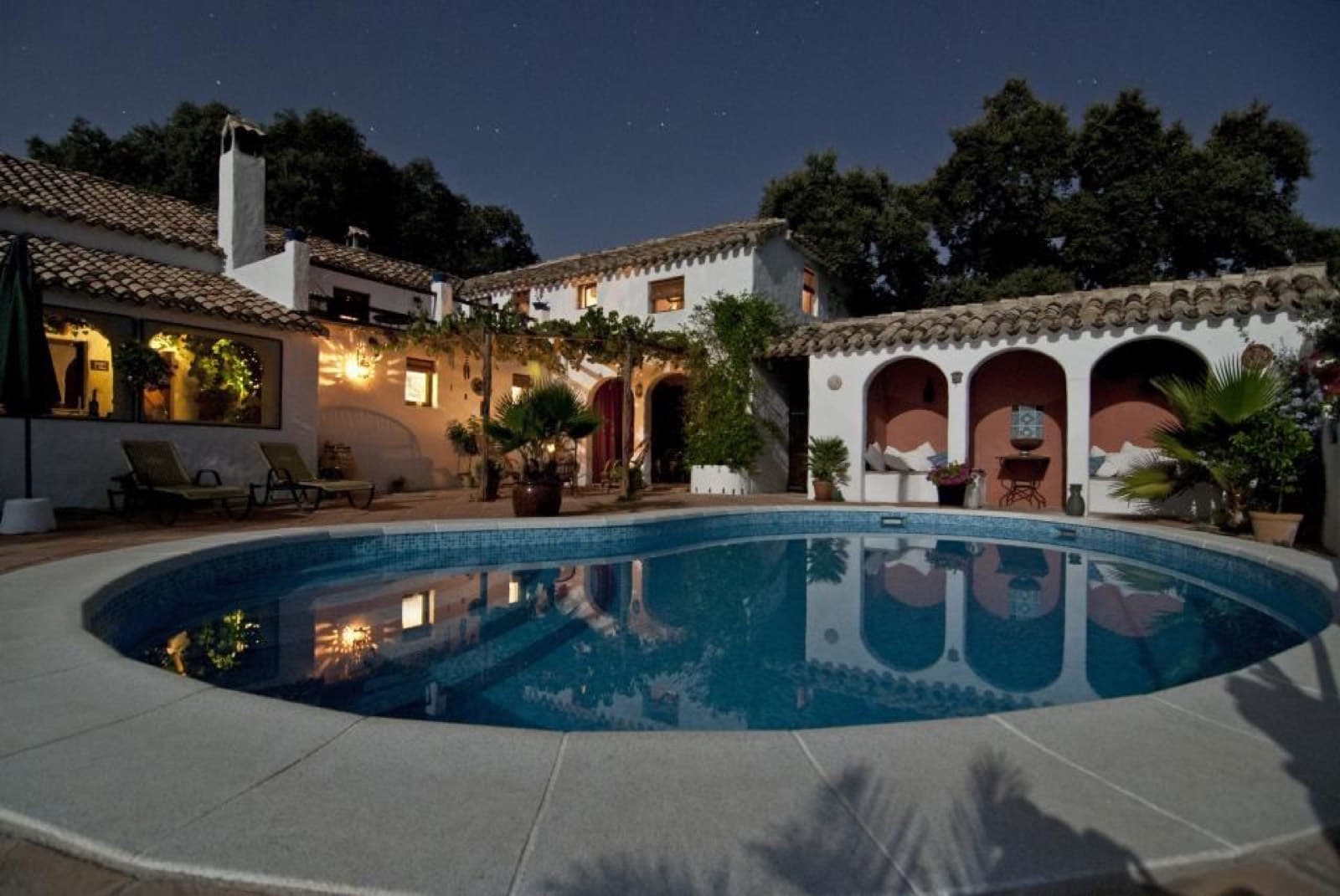 Imagen ilustrativa: alberca redonda iluminada al anochecer frente a una casa de estilo hacienda con arcos y tejas