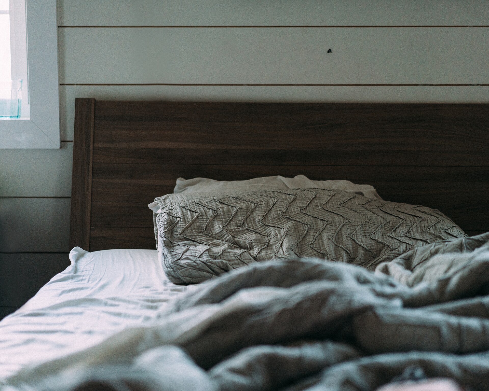 Imagen ilustrativa: recámara con cabecera de madera oscura, ropa de cama gris y pared de tablones blancos