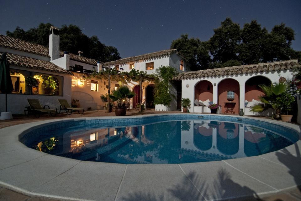 Imagen ilustrativa: alberca redonda iluminada al anochecer frente a una casa de estilo hacienda con arcos y tejas