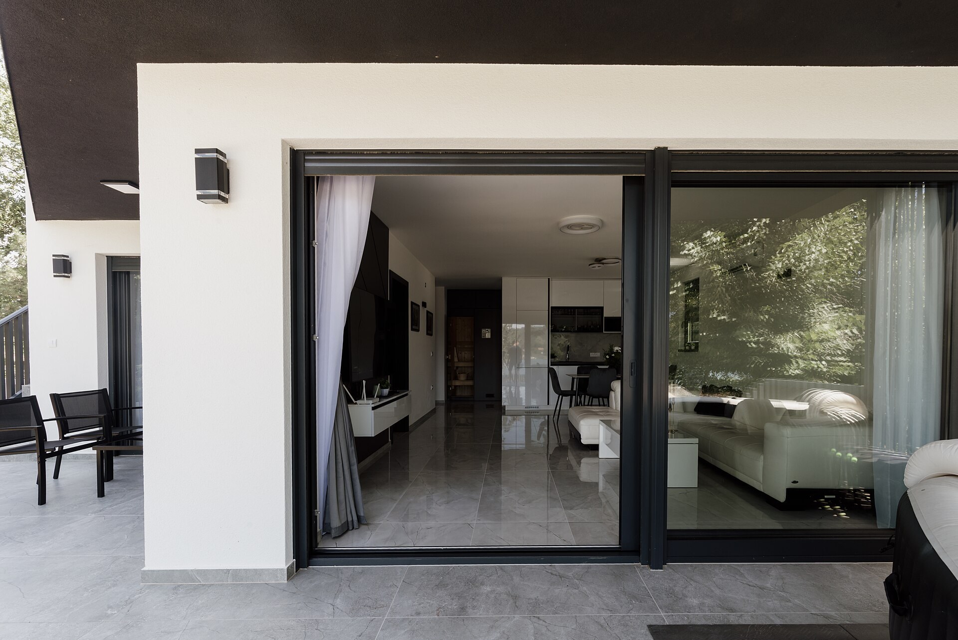 Imagen ilustrativa: fachada moderna blanca con puertas corredizas de vidrio abiertas hacia una sala luminosa y terraza