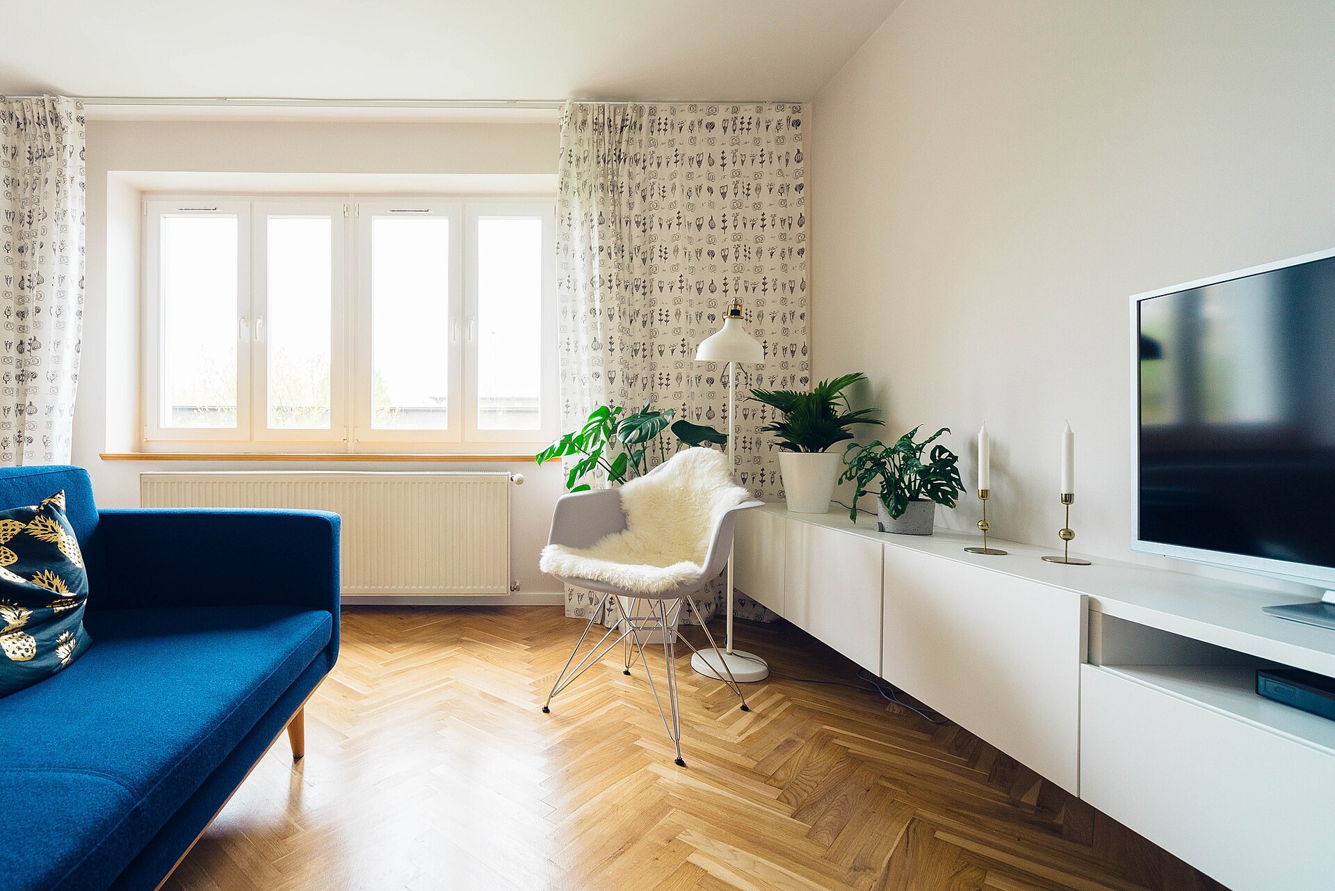 Imagen ilustrativa: sala luminosa con sofá azul, piso de madera en espiga, plantas y mueble blanco