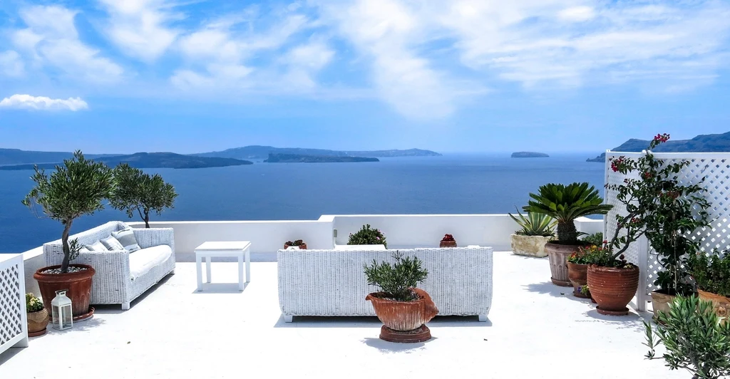 Imagen ilustrativa: terraza blanca con sillones, macetas y vista al mar con islas en el horizonte